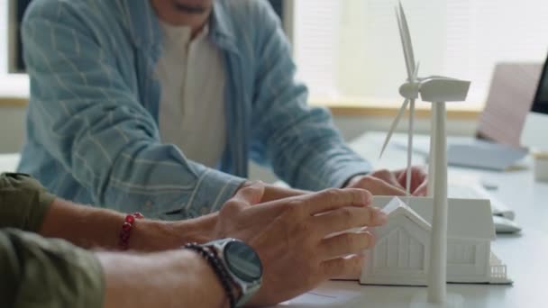 Schnappschuss von zwei männlichen Ingenieuren, die am Bürotisch mit Haus- und Windkraftmakette über Windenergieprojekt diskutieren - Filmmaterial, Video