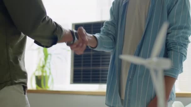 Oříznutý záběr dvou vývojářů obnovitelné energie, kteří si potřásají rukama a diskutují v kanceláři se solárními panely - Záběry, video