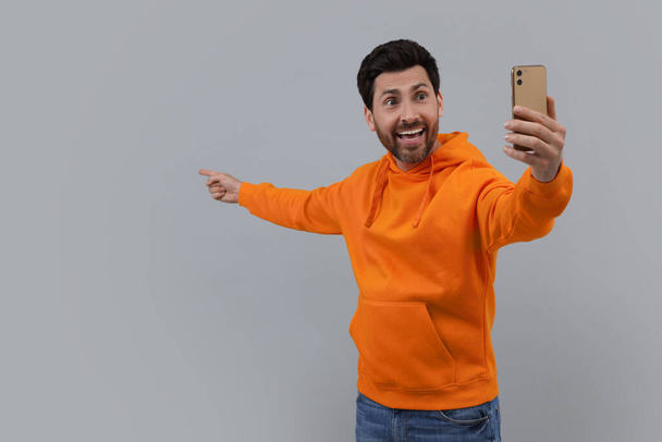Glimlachende man neemt selfie met smartphone op grijze achtergrond, ruimte voor tekst - Foto, afbeelding