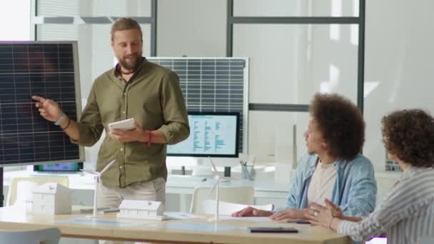Ingegnere delle energie rinnovabili in possesso di tablet digitale e che punta al pannello solare durante la presentazione al team durante la riunione dell'ufficio - Filmati, video