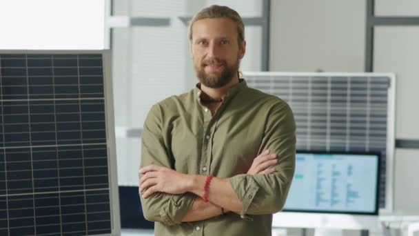 Portrait of professional renewable energy engineer standing beside solar panel in office, holding arms crossed and posing for camera with confidence - Footage, Video