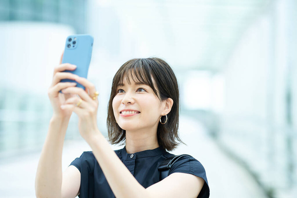 Молодая женщина смотрит на экран смартфона на улице - Фото, изображение