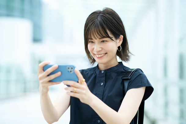 Молода жінка дивиться на екран смартфона на відкритому повітрі - Фото, зображення