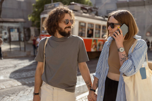Frau telefoniert während ihres Spaziergangs mit ihrem Freund auf der Stadtstraße mit altem Straßenbahnhintergrund  - Foto, Bild