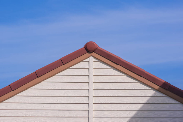 Vista frontal de techo a dos aguas de madera artificial blanca con azulejo de techo marrón de la casa vintage contra fondo de cielo azul - Foto, Imagen