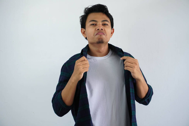Jovem asiático mostrando gesto arrogante ao tocar sua camisa isolada no fundo branco. - Foto, Imagem