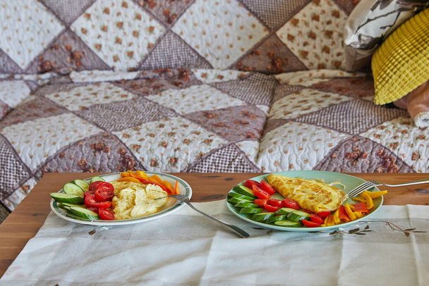 Rano zdrowe śniadanie z jajecznicą z serem parmezanowym, ogórkami, pomidorami wiśniowymi i słodką papryką na stoliku przed kanapą. - Zdjęcie, obraz