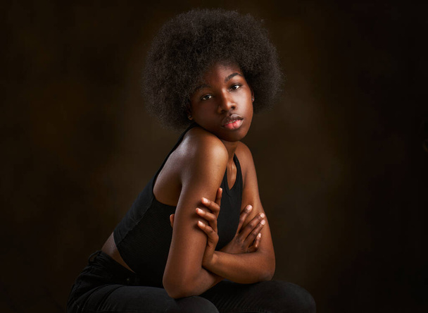 Felice giovane ragazza etnica con acconciatura afro seduta con le braccia incrociate - Foto, immagini
