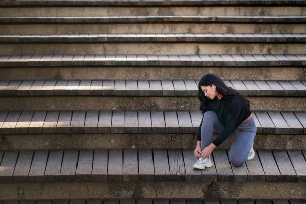 Vista lateral de la joven hembra en ropa casual sentada en las escaleras y mirando hacia otro lado - Foto, imagen