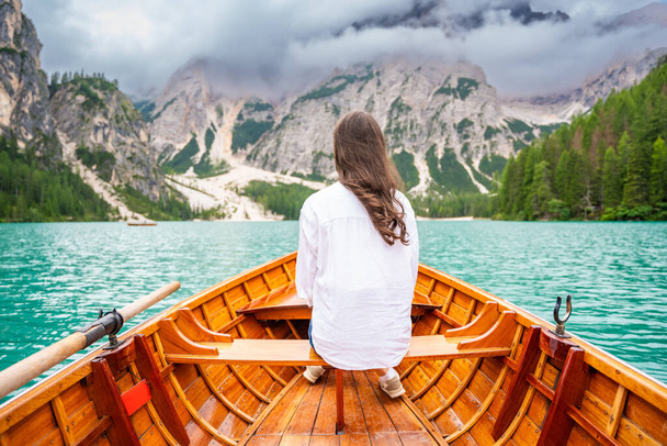 Donna seduta in grande barca marrone al lago di Braies in giornata nuvolosa, Italia. Vacanze estive in Europa. Foto di alta qualità - Foto, immagini