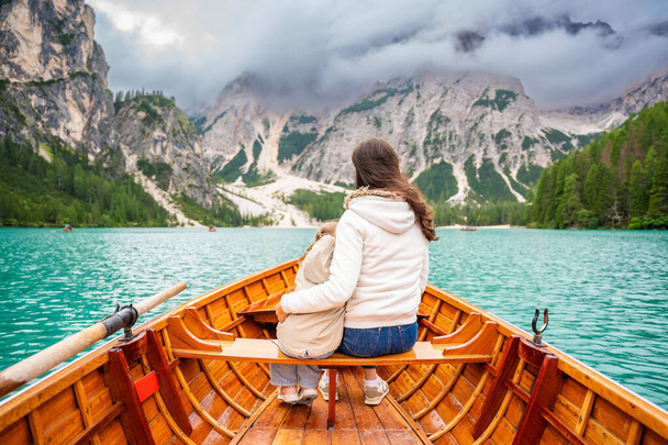 Mulher com sua filha sentada em um grande barco marrom no lago Lago di Braies em dia nublado, Itália. Férias de verão em família na Europa. Foto de alta qualidade - Foto, Imagem