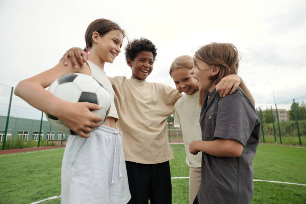 Четверо смеющихся межкультурных друзей, стоящих друг перед другом после игры в футбол и общающихся, наслаждаясь отдыхом после игры - Фото, изображение