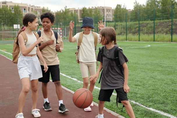 Группа межкультурных одноклассников в спортивной одежде, прогуливающихся по трассе и зеленому футбольному полю на стадионе после школы и беседующих - Фото, изображение