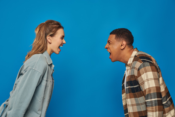 monikulttuurinen pari huutaa toisilleen sinisellä taustalla, väittäen ja väärinkäsitys - Valokuva, kuva