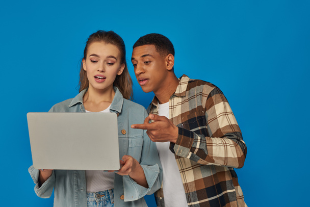 афроамериканський чоловік вказує на ноутбук і обговорює ідеї з колегою-жінкою на синьому фоні - Фото, зображення