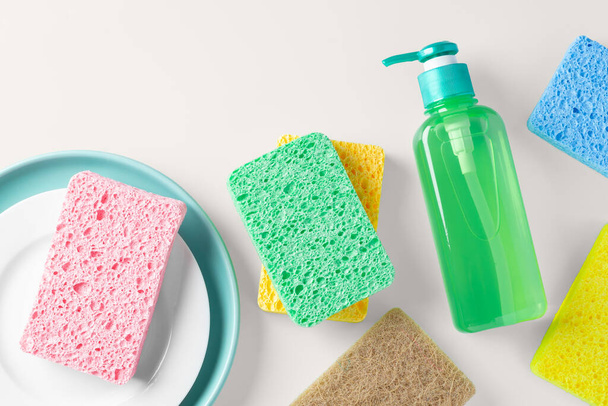 Esponja colorida com prato e sabão de lavar louça verde no fundo bege claro, flat lay - Foto, Imagem