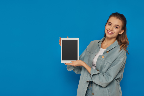 χαρούμενη νεαρή γυναίκα κρατώντας ψηφιακό tablet με λευκή οθόνη στο μπλε φόντο, μέσα κοινωνικής δικτύωσης - Φωτογραφία, εικόνα