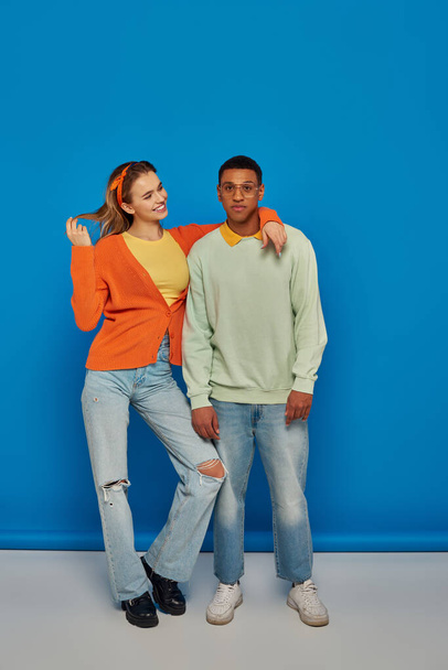 interracial couple in casual attire on blue backdrop, young woman hugging african american man - Foto, imagen