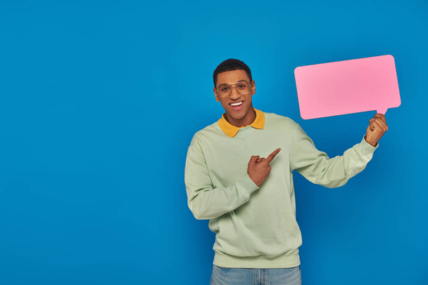 cheerful african american man in eyeglasses pointing at blank speech bubble on blue backdrop - Photo, Image