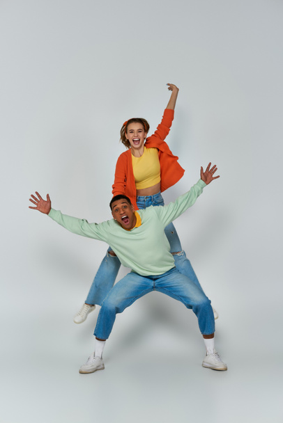 hämmästynyt nuori nainen hyppää korkea lähellä onnellinen afrikkalainen amerikkalainen mies harmaalla taustalla, vapaus ja hauskaa - Valokuva, kuva