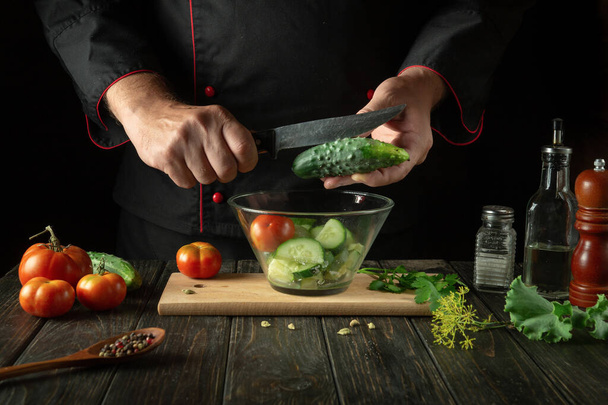 Szef kuchni przygotowuje sałatkę warzywną w kuchni restauracji. Krojenie ogórka nożem do sałatek witaminowych. - Zdjęcie, obraz