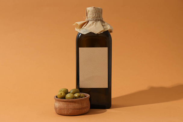 Bottiglia di olio e ciotola di legno con olive su fondo arancione - Foto, immagini