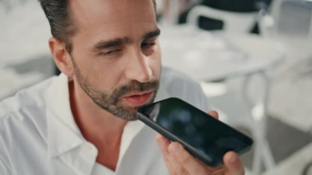 Boss recording audio message for app assistant resting cafeteria closeup. Serious bearded manager talking in telephone loudspeaker at open air place. Hispanic business man making voice sms at cafe  - Footage, Video
