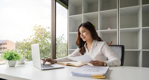 Asiatica donna d'affari utilizzando il computer portatile durante l'analisi di rapporti in ufficio. - Foto, immagini
