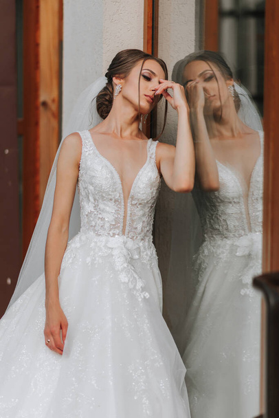 the bride in a wedding dress with a long train and a veil stands near a glass case. Front photo - Fotó, kép