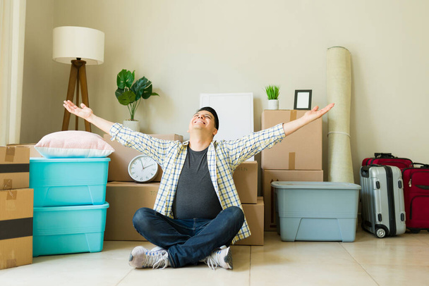 Homem independente animado celebrando ter uma nova casa ou apartamento de aluguel enquanto desempacota um monte de caixas e móveis - Foto, Imagem