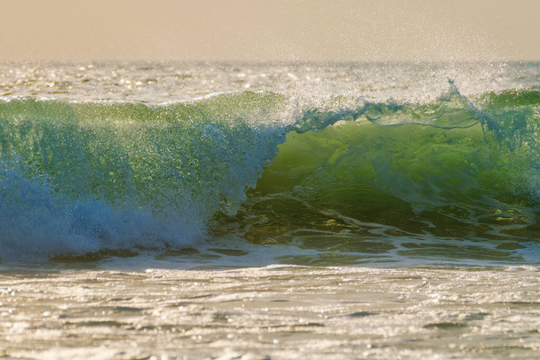 Rompiendo la ola oceánica al atardecer retroiluminado con sol. Fonte da Telha, Costa da Caparica, Portugal - Foto, Imagen