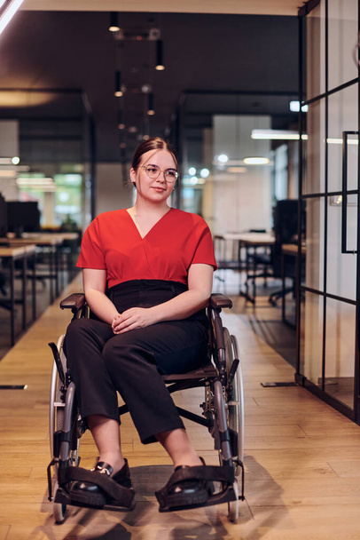 A modern young businesswoman in a wheelchair is surrounded by an inclusive workspace with glass-walled offices, embodying determination and innovation in the business world.  - Foto, Imagem