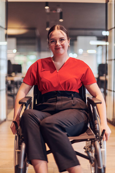 A modern young businesswoman in a wheelchair is surrounded by an inclusive workspace with glass-walled offices, embodying determination and innovation in the business world.  - Zdjęcie, obraz