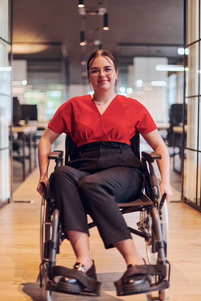 A modern young businesswoman in a wheelchair is surrounded by an inclusive workspace with glass-walled offices, embodying determination and innovation in the business world. - Photo, Image