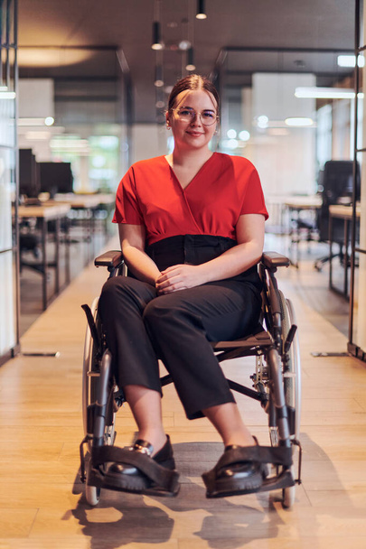A modern young businesswoman in a wheelchair is surrounded by an inclusive workspace with glass-walled offices, embodying determination and innovation in the business world. - Photo, Image