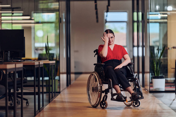 A modern young businesswoman in a wheelchair is surrounded by an inclusive workspace with glass-walled offices, embodying determination and innovation in the business world.  - Fotografie, Obrázek