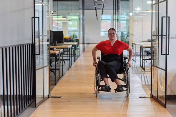 A modern young businesswoman in a wheelchair is surrounded by an inclusive workspace with glass-walled offices, embodying determination and innovation in the business world.  - Photo, image