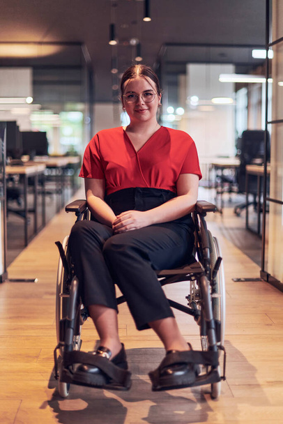 A modern young businesswoman in a wheelchair is surrounded by an inclusive workspace with glass-walled offices, embodying determination and innovation in the business world. - Foto, Imagem