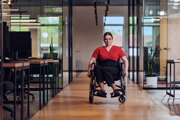 A modern young businesswoman in a wheelchair is surrounded by an inclusive workspace with glass-walled offices, embodying determination and innovation in the business world.  - Фото, изображение