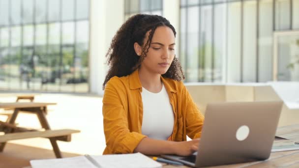 Successful woman employee. Photo of a beautiful positive brazilian or hispanic curly young woman, female student, freelancer, trader, sitting outdoors with laptop and notebook, looks at camera, smile - Πλάνα, βίντεο