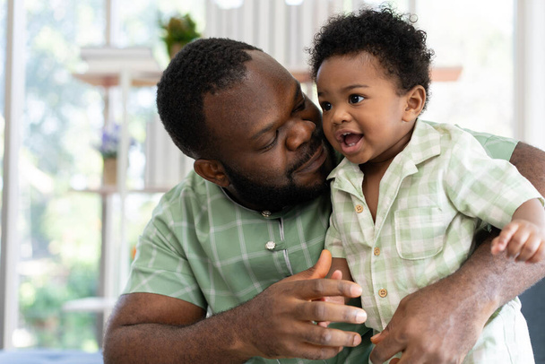 Happy african american man play with little infant toddler child in living room sofa. Parent and little kid relaxing at home. Parents and toddler child girl enjoying spending time at home. Childcare - Photo, Image