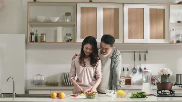 νεαρό ζευγάρι από την Ασία κουβεντιάζοντας κατά την προετοιμασία του γεύματος στην κουζίνα στο σπίτι - Πλάνα, βίντεο