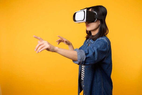 Mujer joven asiática obtener experiencia con el uso de auriculares de realidad virtual juego de entretenimiento aislado en el fondo amarillo. Ganador del concepto de videojuego de futuro cibernético. - Foto, imagen