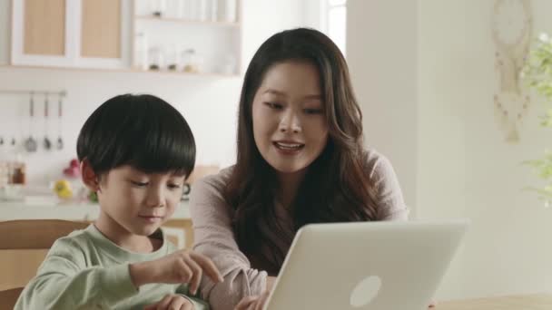 asian mother and son sitting at dining table using laptop computer together at home - Footage, Video
