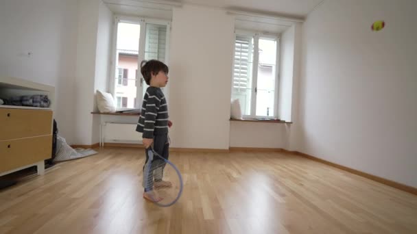 Niño pequeño practicando tenis en casa contra la pared dentro de un dormitorio vacío. Niño golpeando pelota con la coordinación de entrenamiento raqueta - Metraje, vídeo