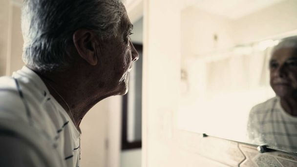 Старший чоловік дивиться на дзеркало у ванній. Літня сіра волосина дивиться на себе - Фото, зображення