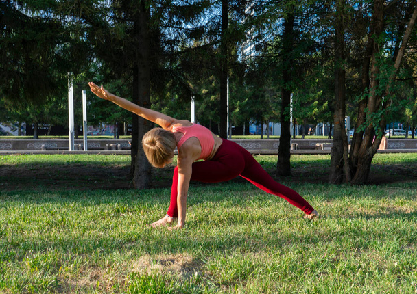 Porträt einer reifen Frau 59 Jahre alt, die Yoga auf der Stadtstraße auf dem Rasen macht. Aktiver Sportlebensstil reifer Menschen.  - Foto, Bild