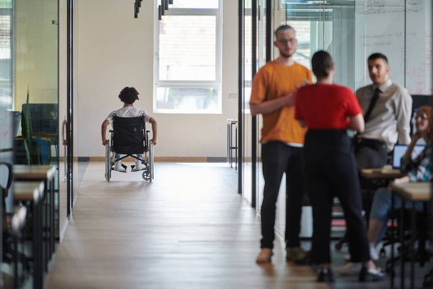 A diverse group of colleagues engages in a discussion about business challenges within a modern coworking startup center, while in the background, their wheelchair-bound colleague symbolizes - Fotó, kép