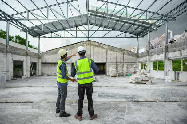 İnşaat mühendisleri ustabaşı veya inşaatçıyla planlar tutarken ve inşaat alanında çelik yapı çatısı altında dururken tartışıyorlar.. - Fotoğraf, Görsel