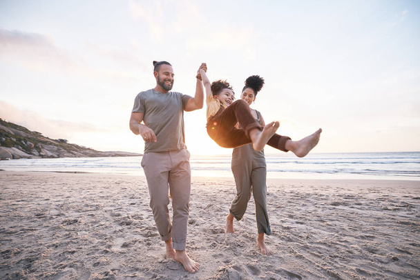 Happy, swing and holding hands with family at beach for bonding, summer vacation and travel. Smile, sunset and relax with parents and child walking on seaside holiday for love, freedom and support. - Photo, Image